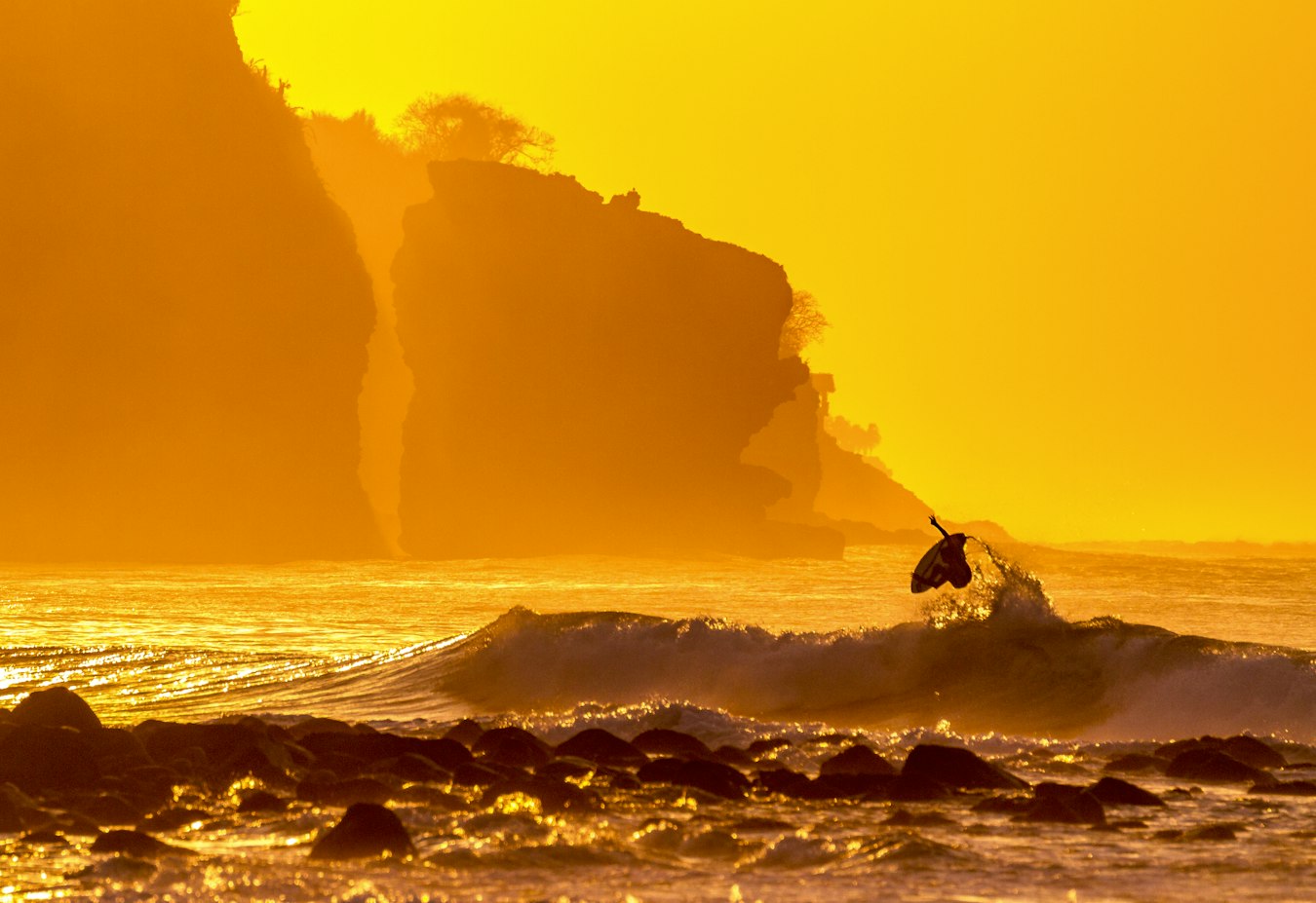 Surfer catching a wave at sunset on a dramatic coastline